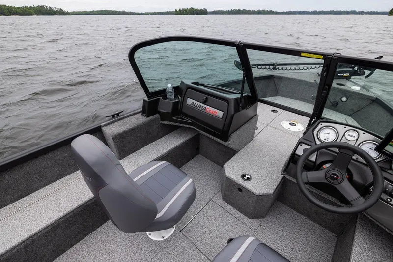 Slide: The Image of 2026 Alumacraft Voyageur 175 Sport boat interior with steering wheel and seating on a lake. - 18