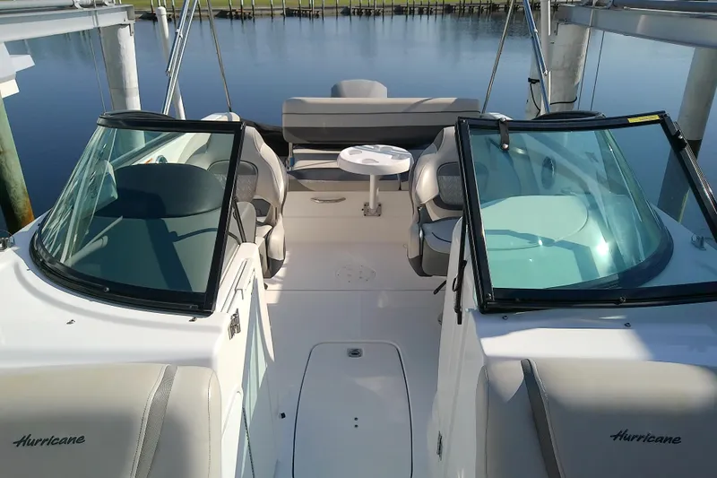 Slide: The Image of 2021 Hurricane SunDeck 2410 OB boat interior with seating and table, docked by calm water. - 10