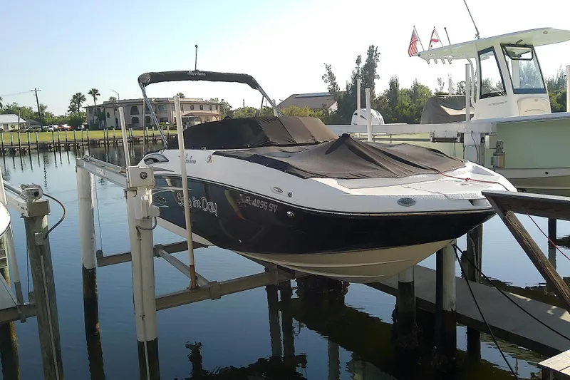 Slide: The Image of 2021 Hurricane SunDeck 2410 OB boat docked on lift, covered, with scenic waterfront backdrop. - 2