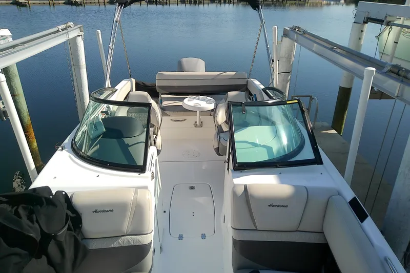 Slide: The Image of 2021 Hurricane SunDeck 2410 OB boat interior with seating and table, docked by calm water. - 4