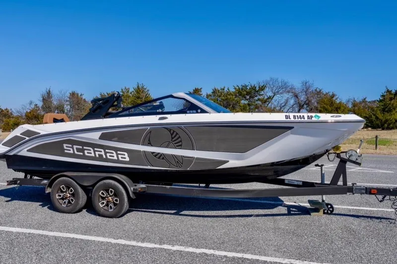 Slide: The Image of 2024 Scarab 235 ID boat on trailer, parked outdoors under clear blue sky. - 6