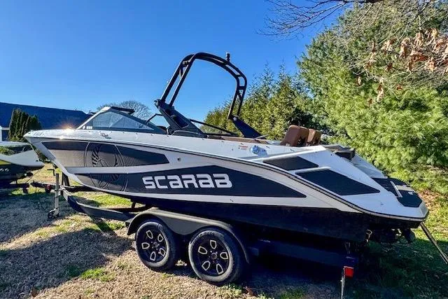 Slide: The Image of 2024 Scarab 235 ID boat on trailer, parked outdoors, surrounded by trees. - 7