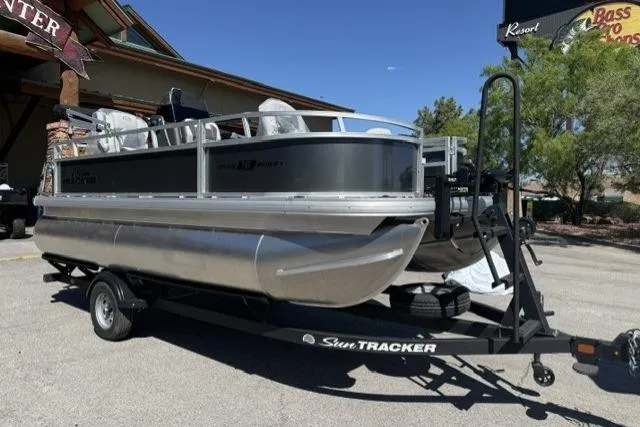 Slide: The Image of 2026 Sun Tracker Bass Buggy 16 XL Select pontoon boat on trailer in outdoor setting. - 1