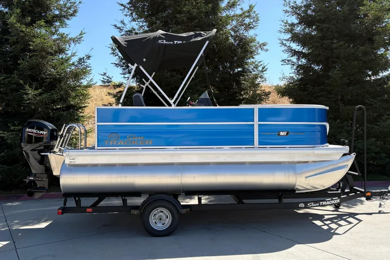 The Image of 2026 Sun Tracker Party Barge 16 DLX pontoon boat on trailer, outdoors. - 0