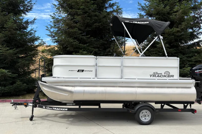 Slide: The Image of 2026 Sun Tracker Party Barge 16 DLX pontoon boat on trailer, surrounded by trees. - 20