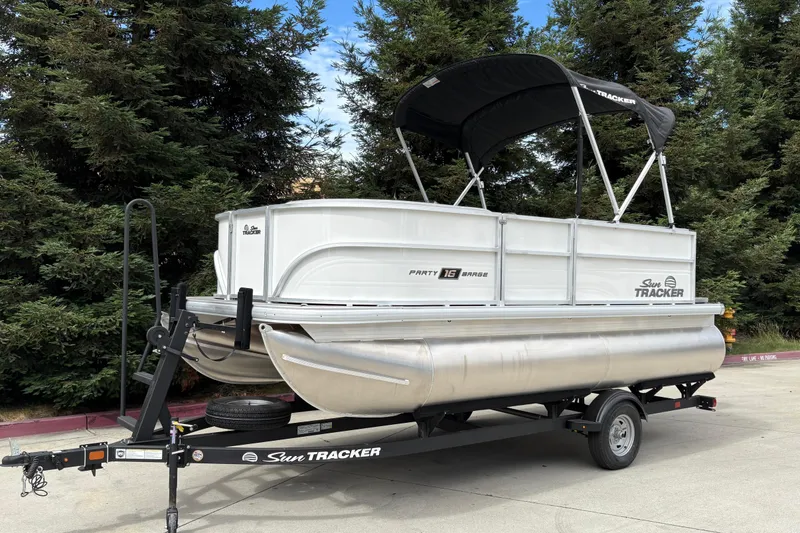Slide: The Image of 2026 Sun Tracker Party Barge 16 DLX pontoon boat on trailer, surrounded by trees. - 22