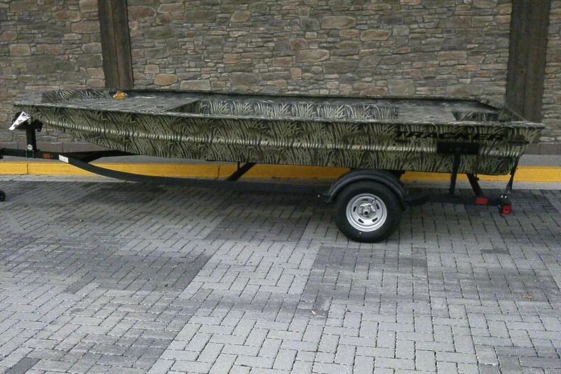 The Image of 2026 Tracker Grizzly 1860 Utility boat on trailer, camo design, parked on brick pavement. - 0