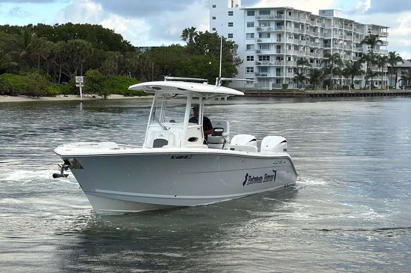 Slide: The Image of 2023 Cobia 280 Center Console boat cruising near waterfront buildings. - 2