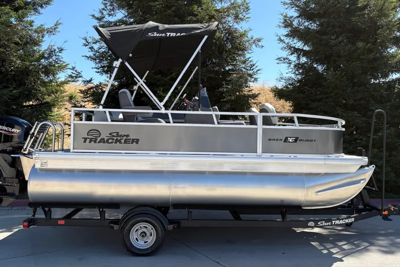 The Image of 2026 Sun Tracker Bass Buggy 16 XL Select pontoon boat on trailer, parked outdoors. - 0