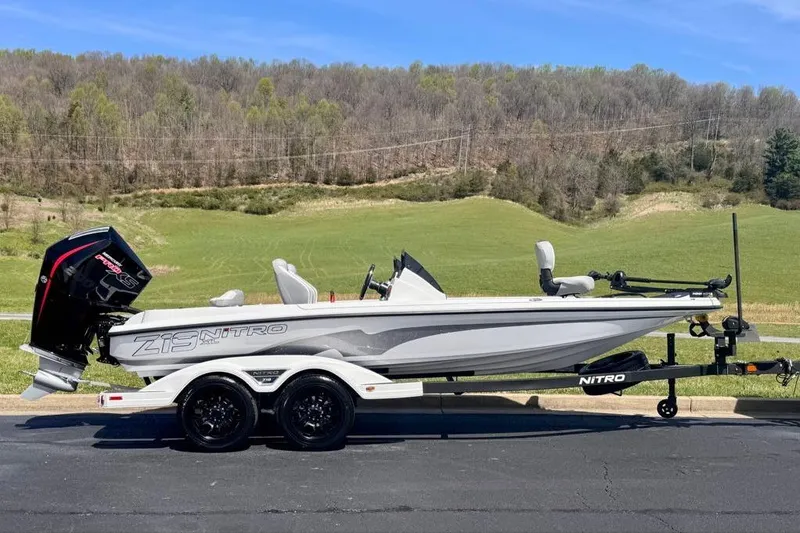 The Image of 2026 Nitro Z19 XL boat on trailer, parked on asphalt with scenic green landscape background. - 0