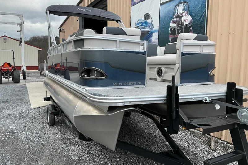 Slide: The Image of 2026 Avalon Venture Quad Lounge 21' pontoon boat on trailer, parked outside a building. - 3