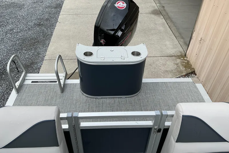 Slide: The Image of 2026 Avalon Venture Quad Lounge boat with outboard motor, docked on concrete and gravel surface. - 9