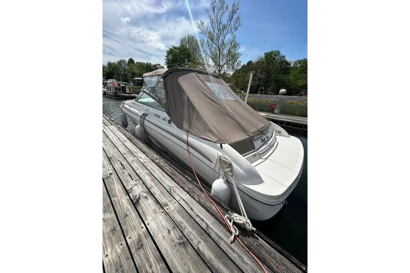 Slide: The Image of 1998 Sea Ray 280 Bow Rider docked, covered, with fenders and ropes, under a clear sky. - 32