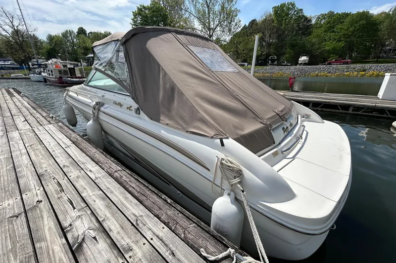 Slide: The Image of 1998 Sea Ray 280 Bow Rider docked with cover, surrounded by calm water and greenery. - 33