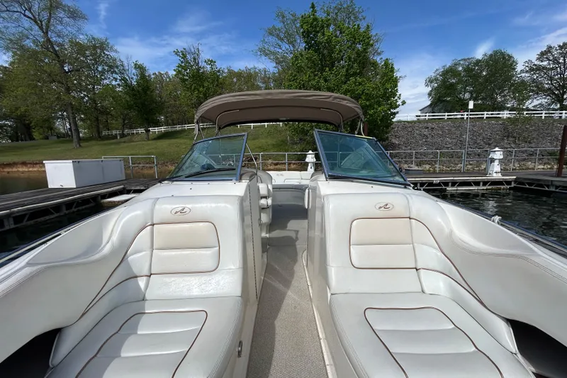 Slide: The Image of 1998 Sea Ray 280 Bow Rider boat interior with white seating, docked by a scenic shoreline. - 52