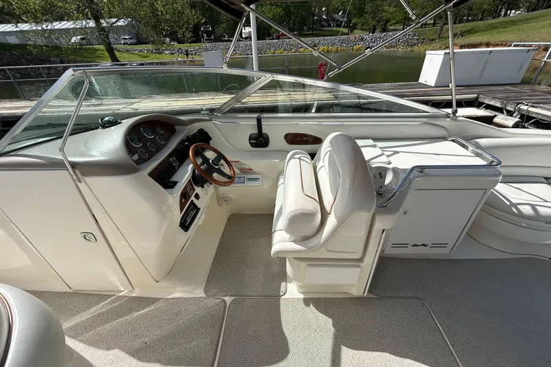 Slide: The Image of 1998 Sea Ray 280 Bow Rider cockpit with steering wheel and seating, docked by a serene lake. - 67