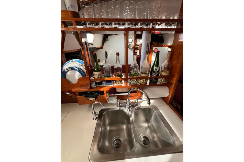 Slide: The Image of 1978 Gulfstar Ketch kitchen with dual sink, glassware, and bottles on wooden shelves. - 31