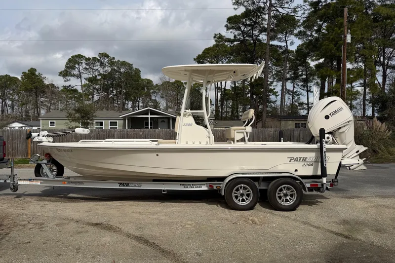 Slide: The Image of 2022 Pathfinder 2200 TRS boat on trailer, parked outdoors with trees in background. - 10