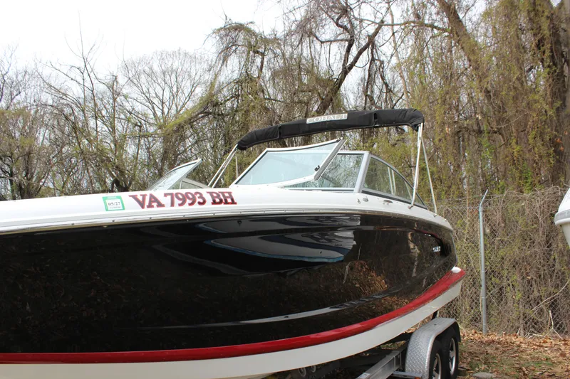 Slide: The Image of 2012 Cobalt A25 boat on trailer, parked near trees and fence. - 2