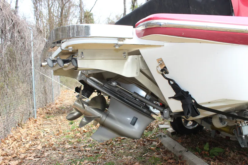 Slide: The Image of 2012 Cobalt A25 boat stern with dual propellers and red trim, parked on leaves. - 43