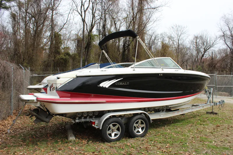 Slide: The Image of 2012 Cobalt A25 boat on trailer, parked outdoors near trees and fence. - 47