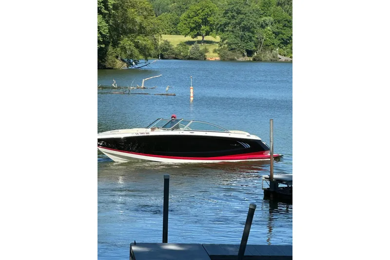 Slide: The Image of 2012 Cobalt A25 boat cruising on a serene lake with lush green surroundings. - 48