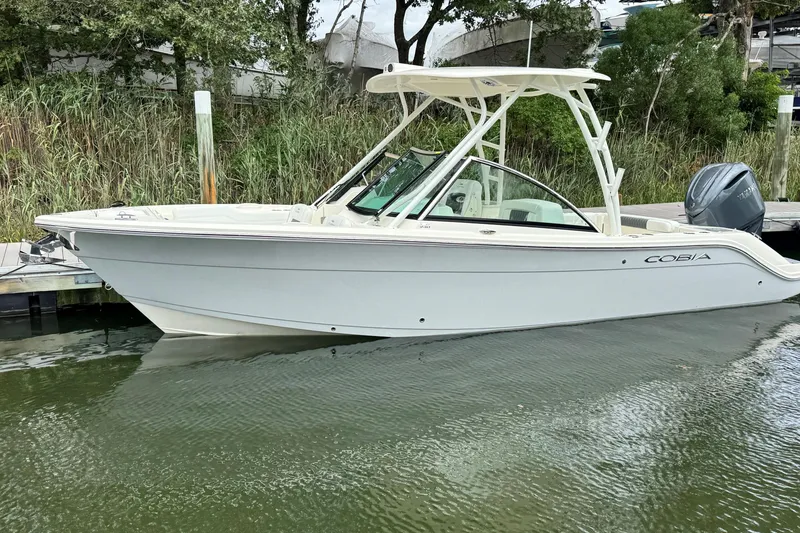 The Image of 2026 Cobia 240 Dual Console boat docked on calm water, surrounded by greenery. - 0