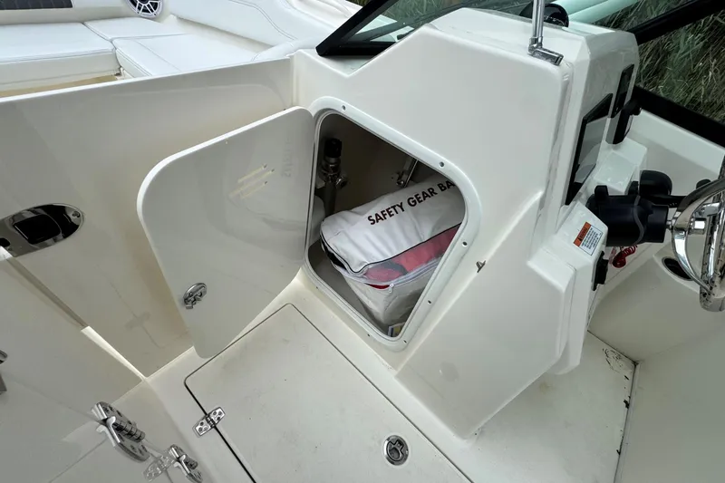 Slide: The Image of 2026 Cobia 240 Dual Console boat with open storage compartment and safety gear bag. - 13