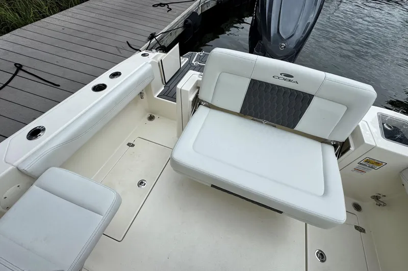 Slide: The Image of 2026 Cobia 240 Dual Console boat interior with white seating and dockside view. - 8