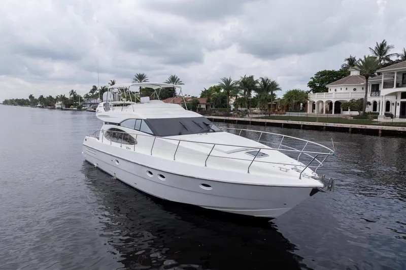 Slide: The Image of 1999 Azimut 58 yacht cruising on a calm waterway, surrounded by luxury homes and palm trees. - 2