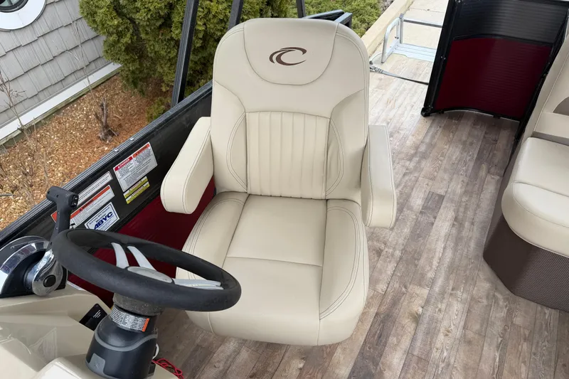 Slide: The Image of Captain's chair and steering wheel on 2018 Crest I boat, featuring beige upholstery and wood-style flooring. - 10