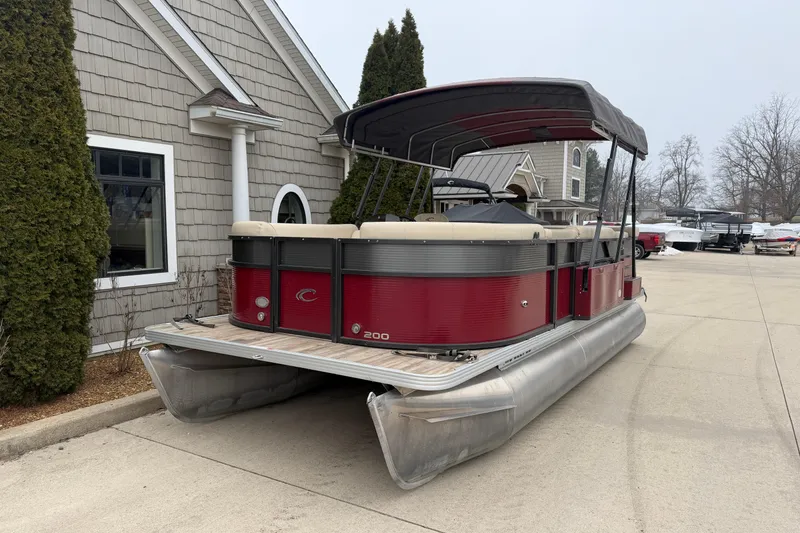 Slide: The Image of 2018 Crest I pontoon boat with red exterior, parked near a house. - 2