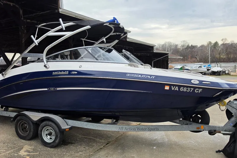 The Image of 2014 Yamaha Boats 242 Limited on trailer, dockside, with blue and white exterior. - 0