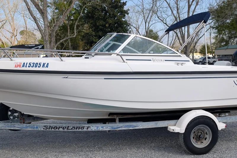 The Image of 1998 Boston Whaler Ventura 20 boat on trailer, parked outdoors with trees in background. - 0