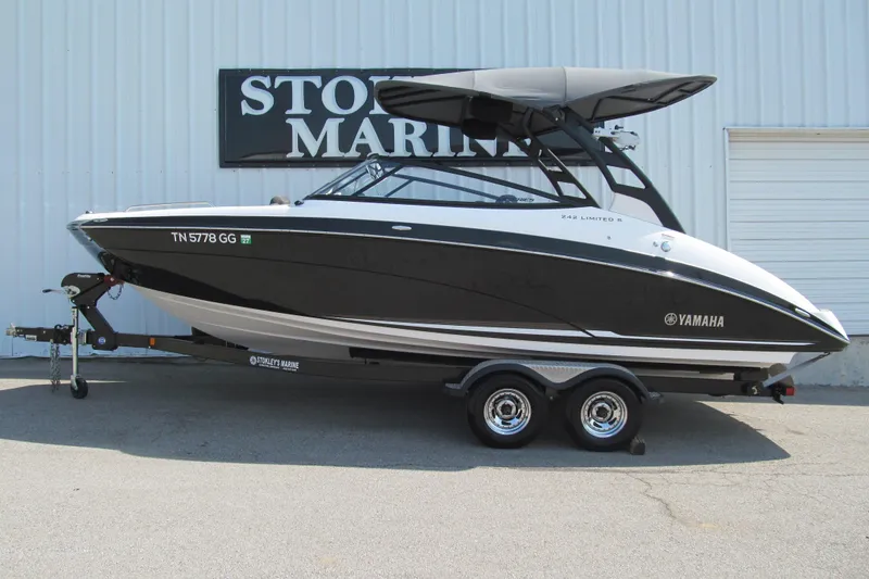 The Image of 2018 Yamaha Boats 242 Limited S on trailer, black and white design, parked outside marine store. - 1