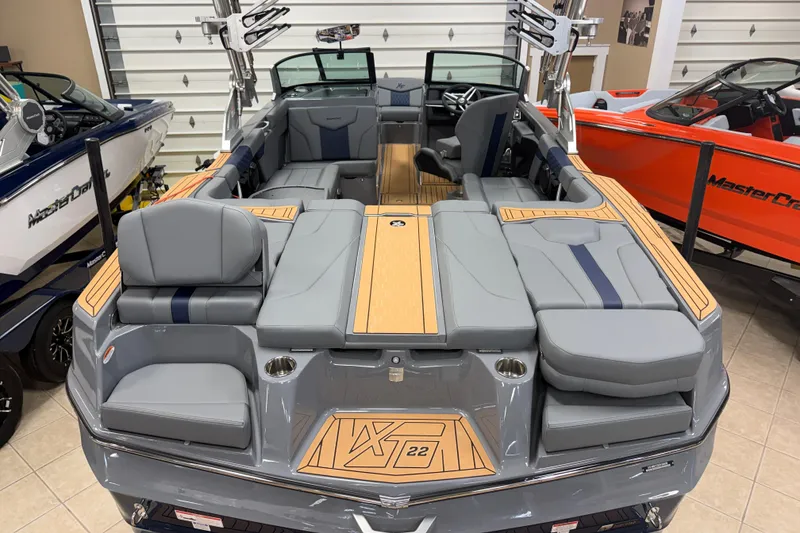 Slide: The Image of 2026 MasterCraft XT22 boat interior with gray seating and wood accents in showroom. - 2