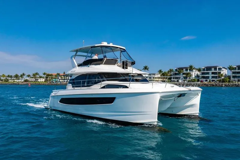 Slide: The Image of 2024 Aquila 44 Yacht cruising on blue water near modern waterfront homes. - 2