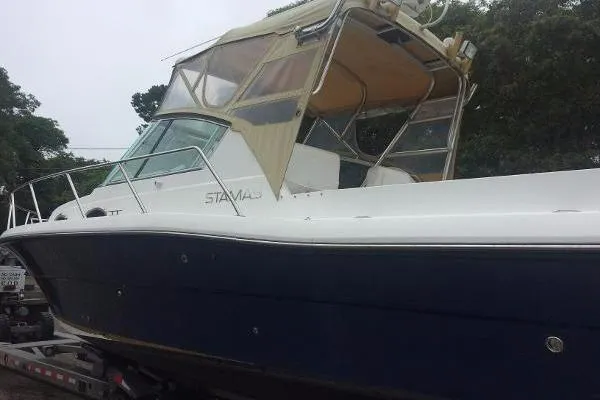 Slide: The Image of 2000 Stamas 310 Express boat with a blue hull and beige canopy on a trailer. - 2