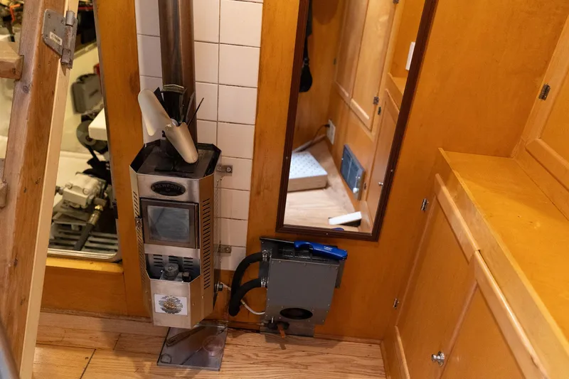 Slide: The Image of Interior of a 1997 Custom Steel Trawler featuring a compact wood stove and wooden cabinetry. - 21