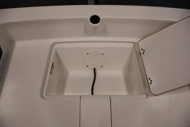 Slide: The Image of 2022 Mako Pro Skiff 17 CC storage compartment with open lid and drainage hole. - 11
