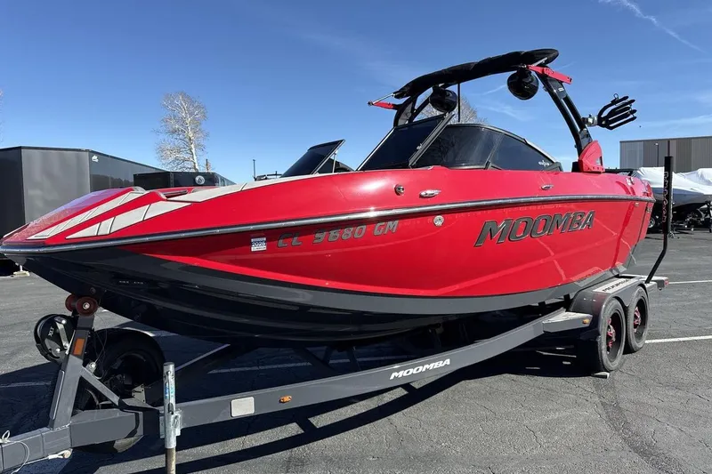 The Image of Red 2022 Moomba Mojo boat on trailer, parked outdoors under clear blue sky. - 1