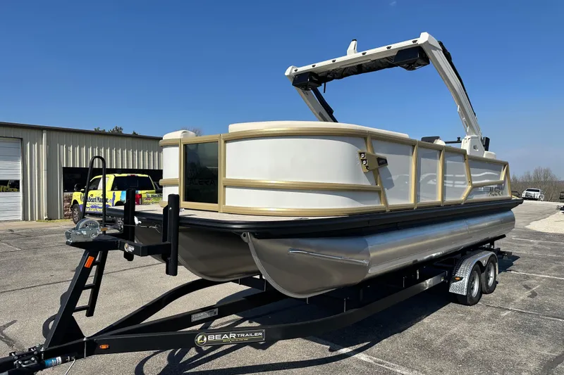 Slide: The Image of 2026 Alera M23Q pontoon boat on trailer, parked outdoors under clear blue sky. - 1
