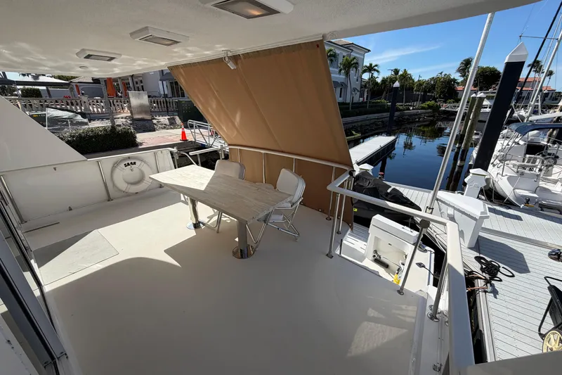 Slide: The Image of 1991 Hatteras 70 Motor Yacht docked, featuring spacious deck and covered seating area. - 32