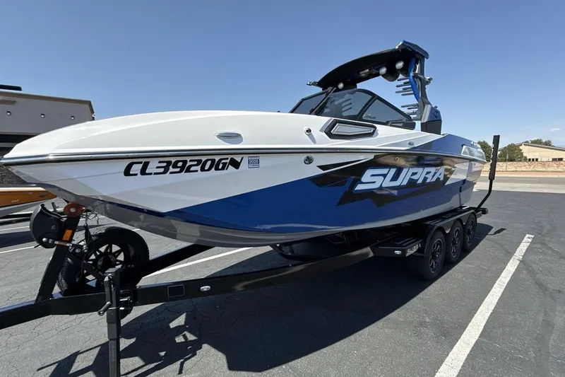 The Image of 2023 Supra SE 550 boat on trailer, blue and white design, parked outdoors. - 1