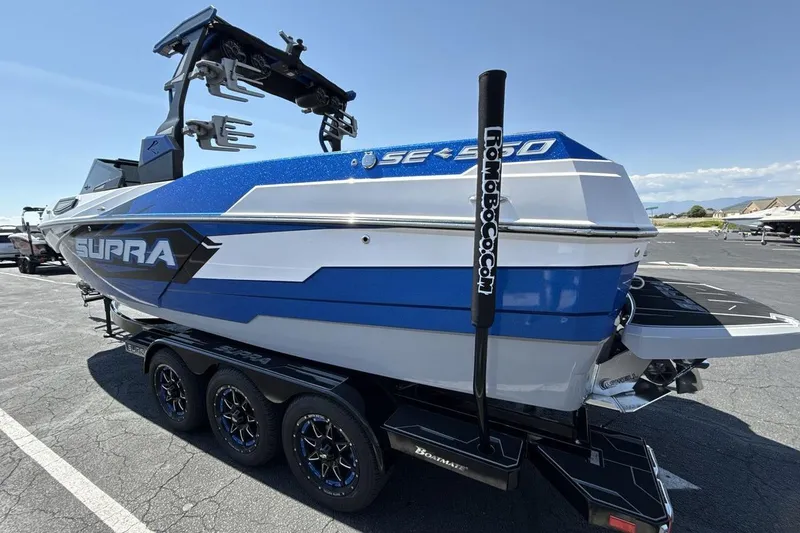Slide: The Image of 2023 Supra SE 550 boat on trailer, blue and white design, parked outdoors. - 3