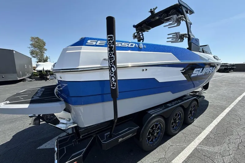 Slide: The Image of 2023 Supra SE 550 boat in blue and white, parked on a trailer in a lot. - 5