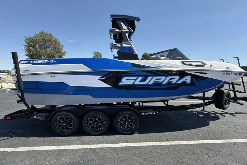 Slide: The Image of 2023 Supra SE 550 boat on trailer, blue and white design, parked outdoors. - 6