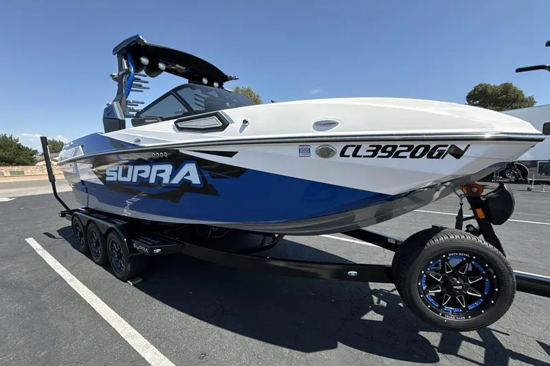 Slide: The Image of 2023 Supra SE 550 boat on trailer, blue and white design, parked outdoors. - 7