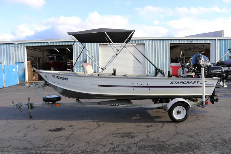 Slide: The Image of 1997 Starcraft Patriot 160 boat on trailer, parked outside a blue warehouse. - 3