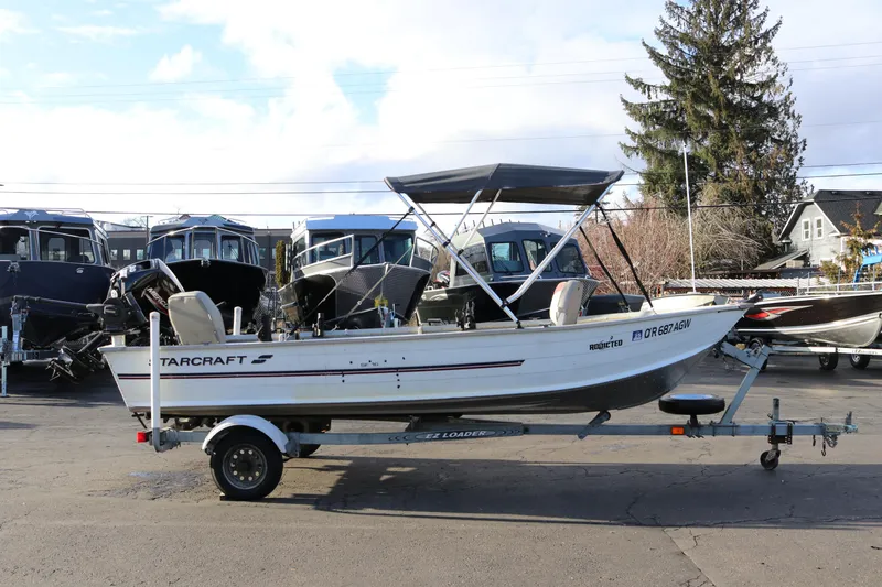 The Image of 1997 Starcraft Patriot 160 boat on trailer, parked outdoors with other boats in background. - 1